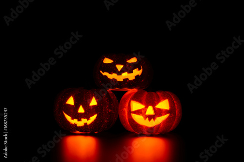 Three spooky carved pumpkins on table in darkness