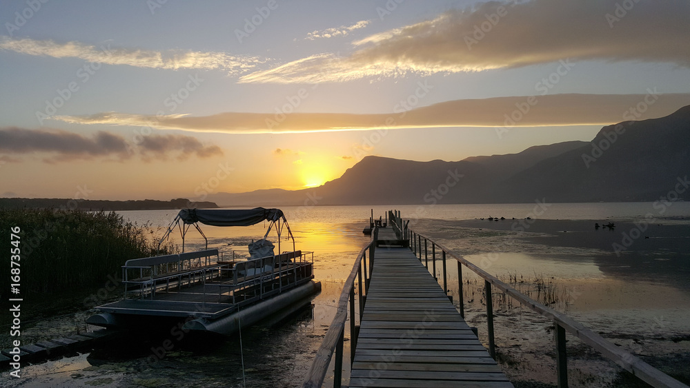 Boat and pier on lake against sunset and mountains.