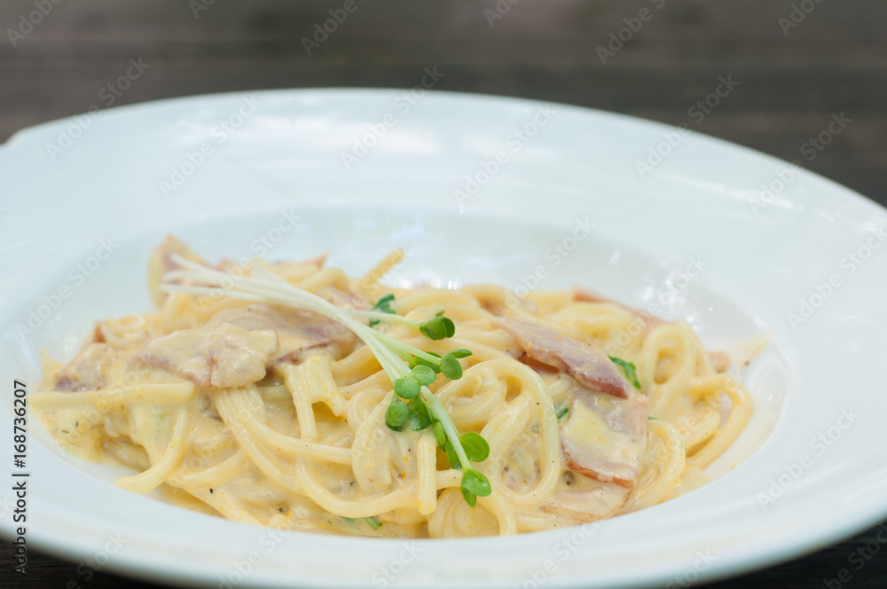 Carbonara spaghetti with ham in white plate on wooden table.