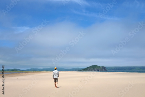 Man walking along the sand beach to the sea