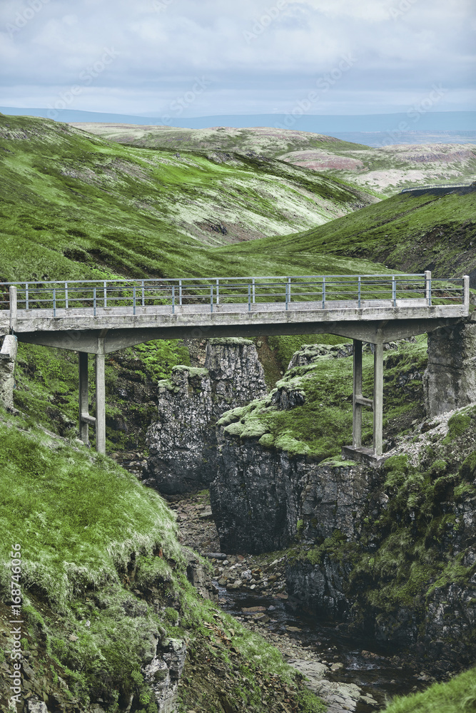 the old stone bridge over the gorge with a stream in the mountains in Iceland
