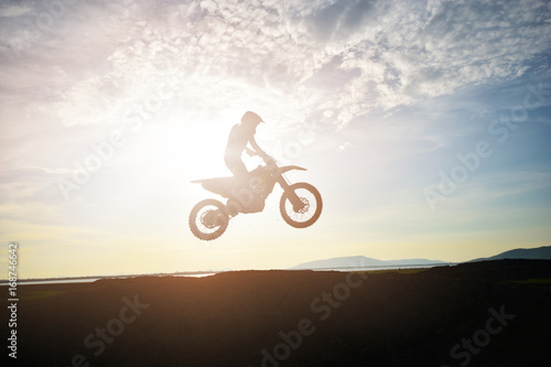 The silhouette of a motorcycle motocross jump from the hill at sunset.