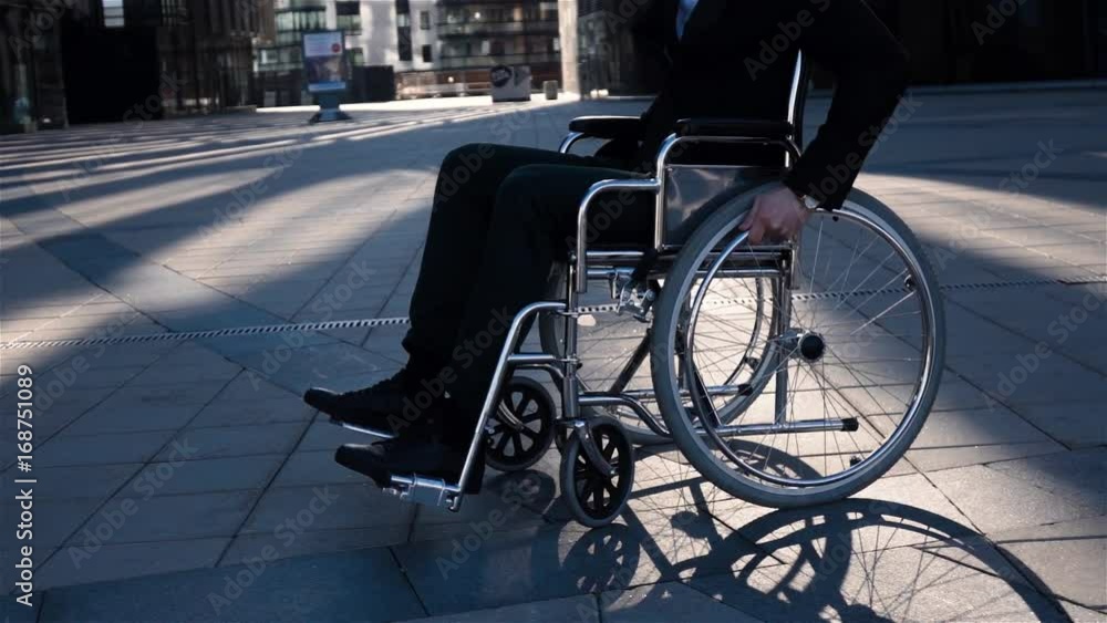 Slow motion shot of a businessman with in wheelchair walking and turning around and look at camera on the business district square. Happy smiling disabled man. Middle view Slow motion shot of a businessman with in wheelchair walking and turning around and look at camera on the business district square. Happy smiling disabled man. Middle view