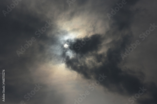 雲から透けて見える太陽「空想・雲のモンスターたち〔左のグレーの雲のモンスター（太陽が目）と右の黒雲のモンスターが衝突し、黒雲のモンスターの顔や体が大きくぶれるイメージ〕」衝突、お互い前を見て進もう！、安全運転、前方注意！、横顔に体当たり、ぶつかるなどのイメージ