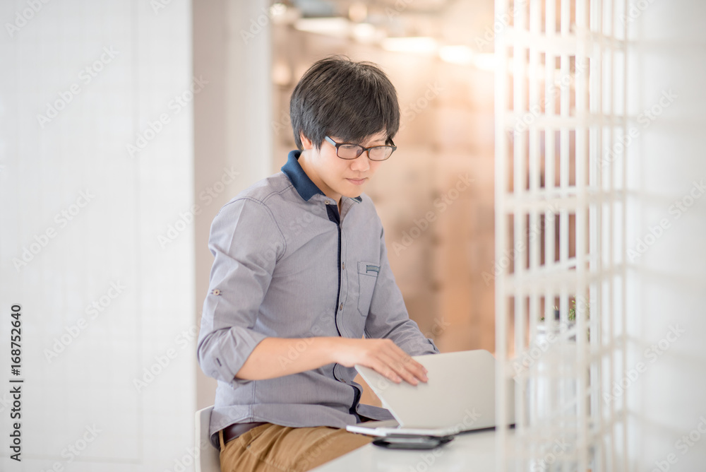 Young Asian man dressed in casual style working in cafe with his laptop computer. Digital nomad and IT modern lifestyle, Co working space for freelance jobs Young Asian man dressed in casual style working in cafe with his laptop computer. Digital nomad and IT modern lifestyle, Co working space for freelance jobs