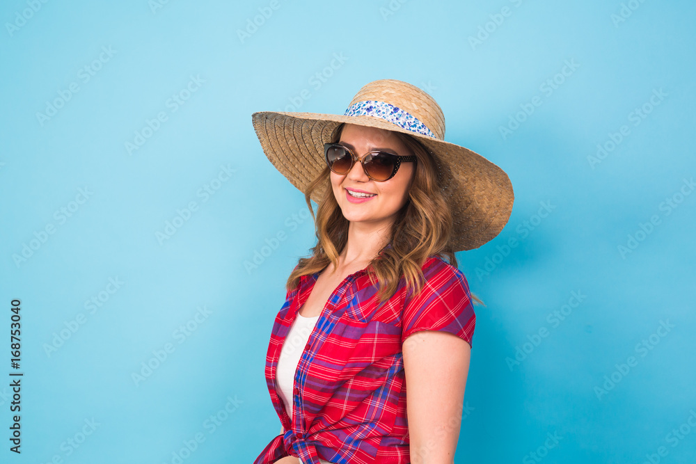 Beautiful young woman wears in summer dress and straw hat is laughing on blue background with copy space