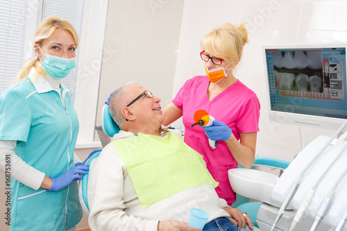 Old Senior man on the operation in the dental office. Dentist with assistant examining implants teeth