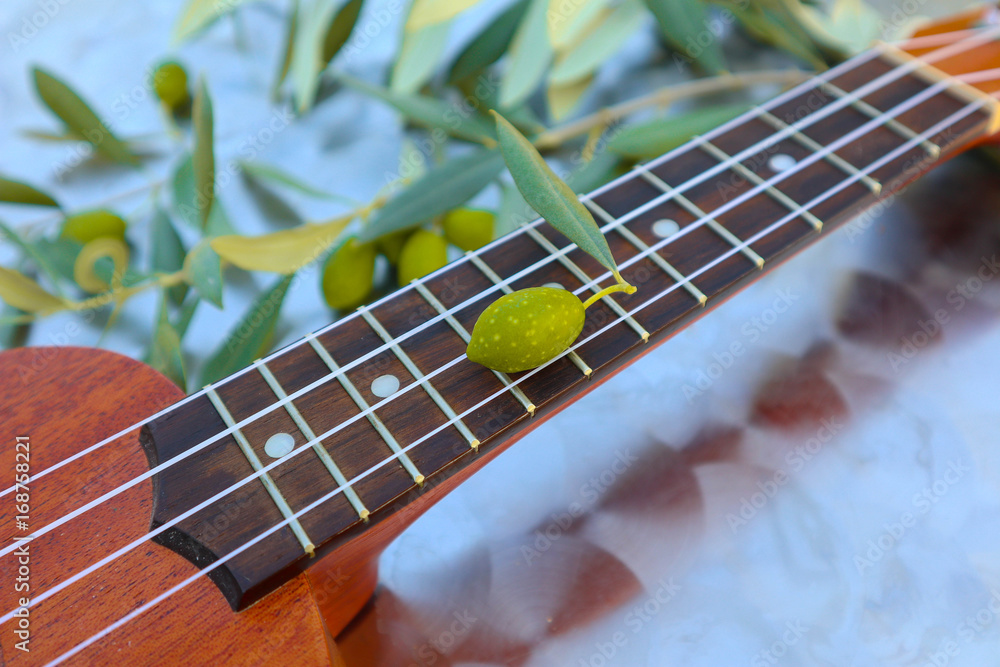 Obraz premium Olive brunches and ukulele, Greek music concept close up. Small guitar under the olive tree, Greece melody backdrop.