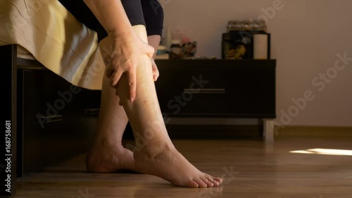 Senior woman sitting on bed doing self legs massage in her bedroom