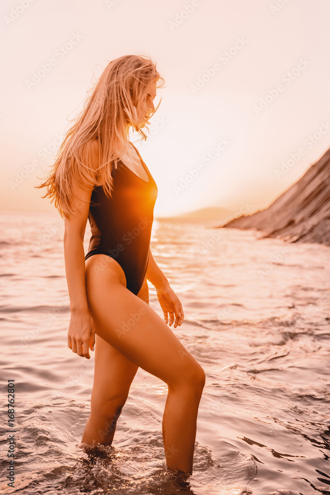 Blonde woman in black swimwear relaxed on beach and quiet sea with warm sunset colors. Blonde woman in black swimwear relaxed on beach and quiet sea with warm sunset colors.