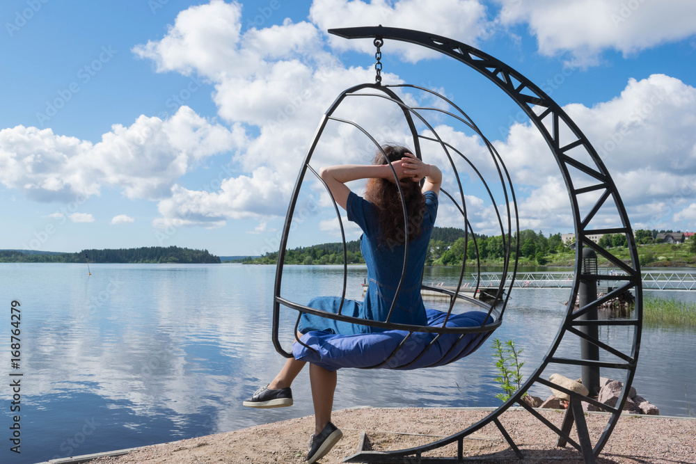 Young woman relaxing sitting on a swing next to the lake. Young woman relaxing sitting on a swing next to the lake.