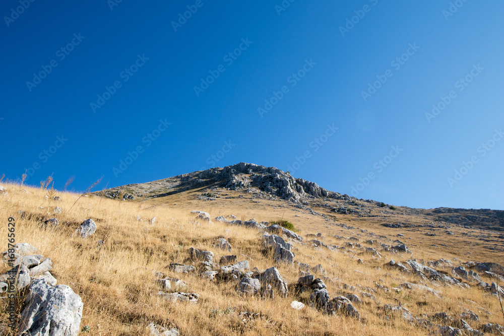 Rocky mountain with yellow grass fields and blue sky in the background. Peak of Marsicano mountain in Abruzzo