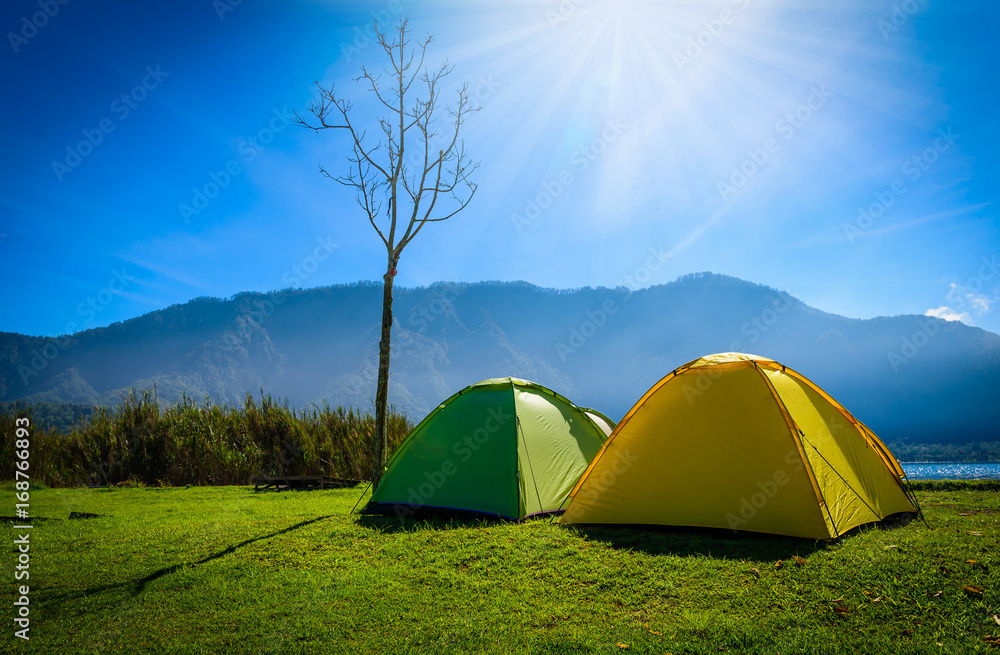 Yellow and green camping tent on grass near mountain river in morning the summer day.