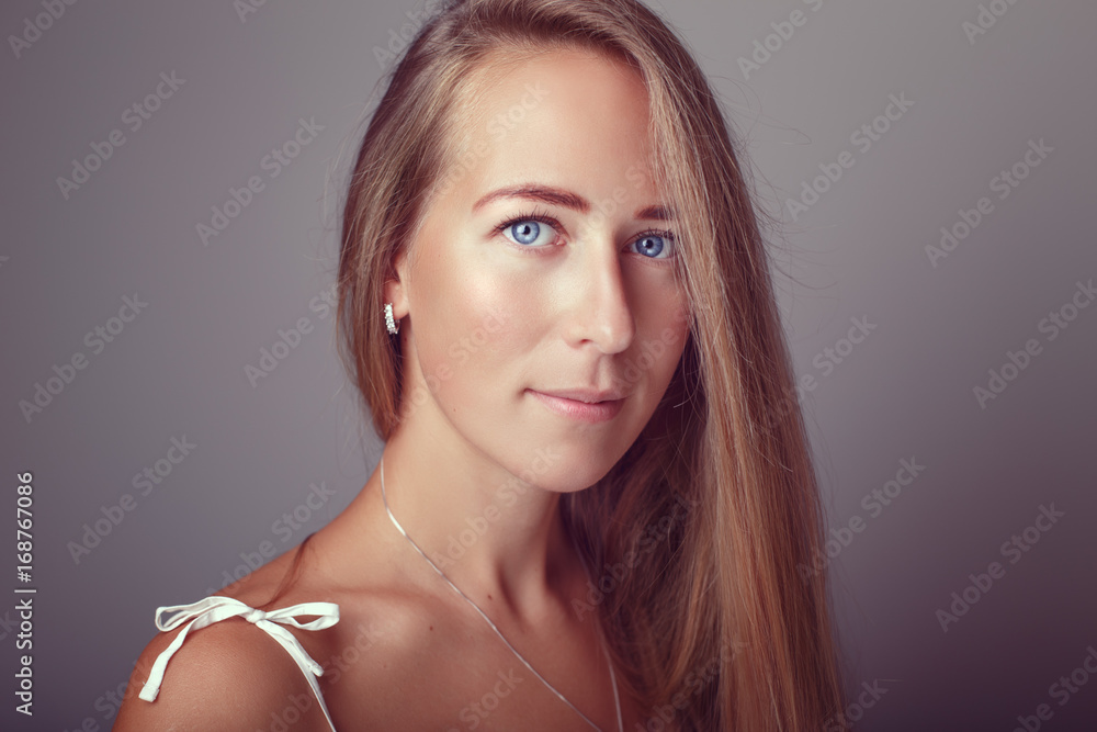 Portrait of calm pensive Caucasian blonde young beautiful girl woman model with long hair and blue eyes in white dress. Slav european model posing in studio on plain light background.