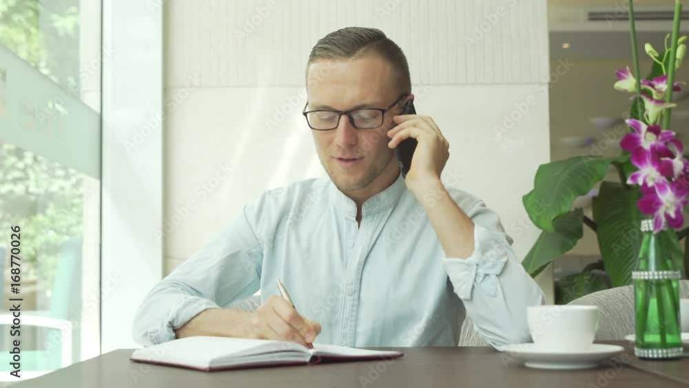 Businessman writing in daily planner while speaking on cellphone Businessman writing in daily planner while speaking on cellphone