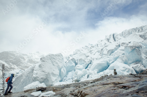 A small man  person explores a glacier and is walking up to the glacier