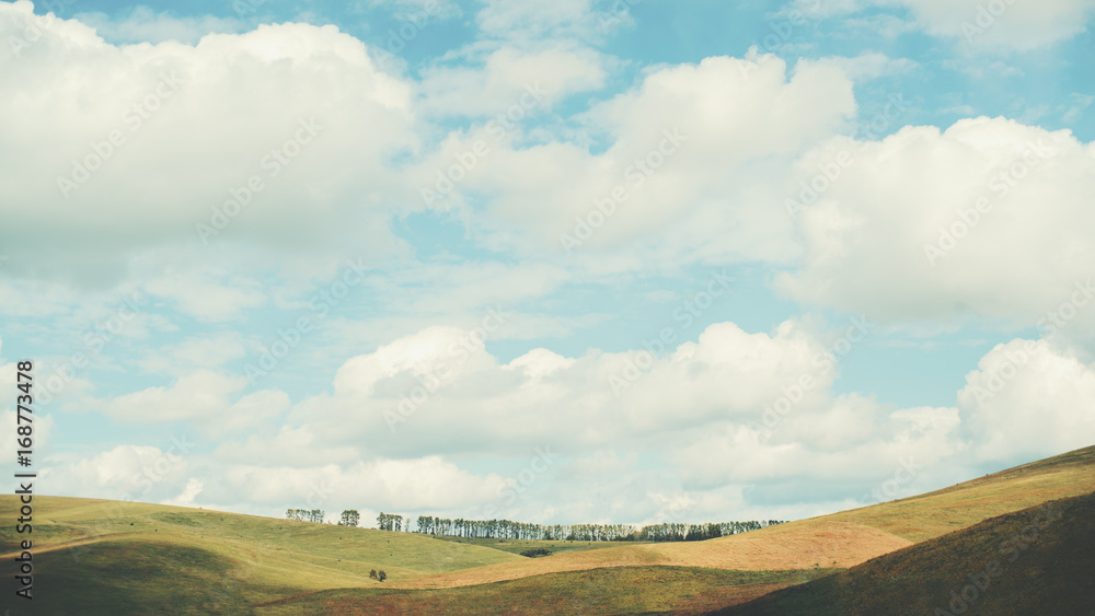 Stunning bright landscape: beautiful low hills lit by morning sun through amazing cloudscape which is casting shadows on the ground, teal sky, Altai mountains, Russia