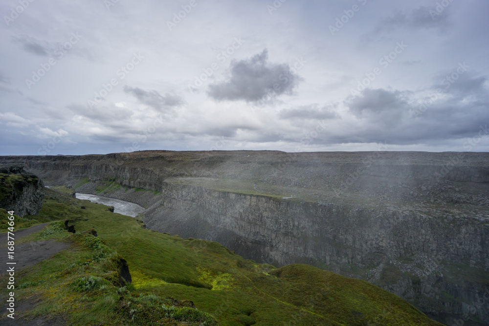 Iceland - Giant canyon of detifoss waterfall with river flowing beneath green moss covered area