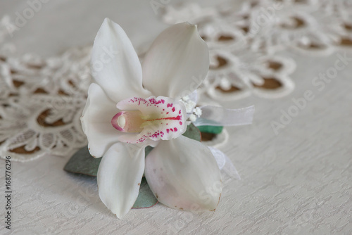 White orchid boutonniere small bouquet for buttonhole used for groom and wedding guests positioned on a white cloth  in natural light