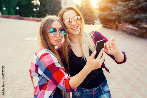 Portrait of a happy two smiling girls making selfie photo on smartphone. urban background. The evening sunset over the city.