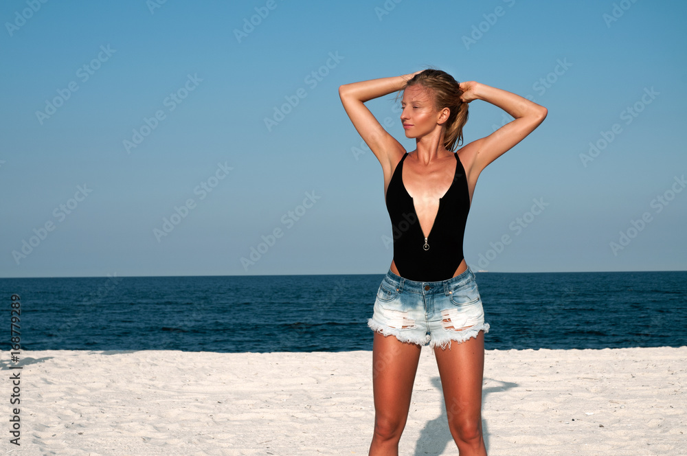 Beautiful woman in black swimsuit and jeans shorts on the beach. Beautiful woman in black swimsuit and jeans shorts on the beach.