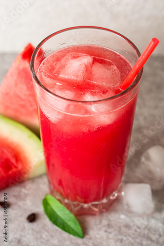 Fresh watermelon smoothie with ice and mint in glass on gray stone background