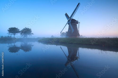 Dutch windmill by lake in dusk