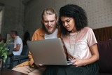 Portrait of young man and girl amazedly looking at laptop. African American girl with dark curly hair sitting with friend at cafe. Surprised boy and girl sitting in restaurant with laptop in hands