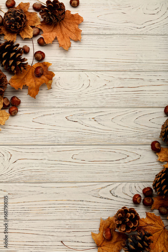 Flat lay frame of autumn leaves, cones and nuts on a wooden background.