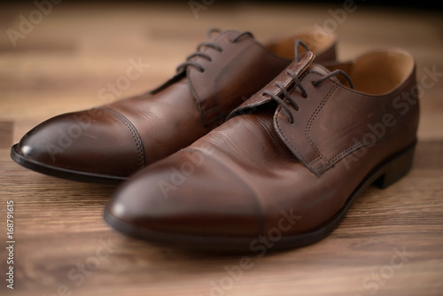 Elegant used brown leather male shoes set on a brown wooden table.