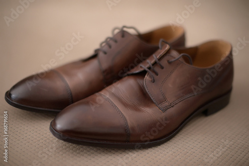 Elegant used brown leather male shoes set on a solid beige background with vignette effect