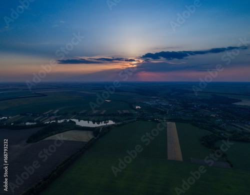 Beautiful panoramic aerial view of the valley with green fresh fields and meadow at sunset. Twilight above the village with a lake