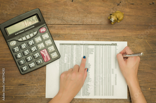 Mão de mulher analisando planilha de custos, utilizando calculadora, trabalhando, visto de cima  photo