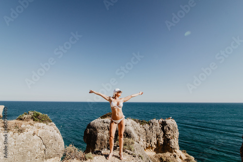 Woman tourist wears hat, bikini, raises hands up and enjoys summertime with background