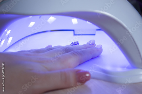 Professional ultraviolet nail manicure lamp drying gel polishing on woman's hand in a beauty salon photo
