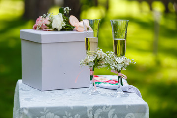 Two wineglasses with pink ribbon and gift box on a table on wedding ceremony