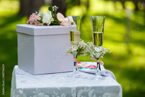 Two wineglasses with pink ribbon and gift box on a table on wedding ceremony