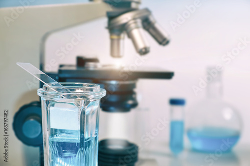 Scientific, medical or education background. Biological or biochemical lab out of focus, closeup on glass Coplin jar with tissue sections in staining solution. photo