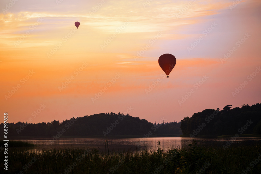 hot air balloon over a lake and forest landscape in the evening sky at sunset,  leisure activity and beautiful nature experience