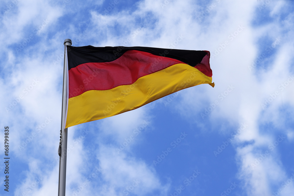 Flag of Germany with stripes in red, black and gold, national symbol or sign of the european country, fluttering in the wind against the blue sky with clouds on a sunny day Flag of Germany with stripes in red, black and gold, national symbol or sign of the european country, fluttering in the wind against the blue sky with clouds on a sunny day