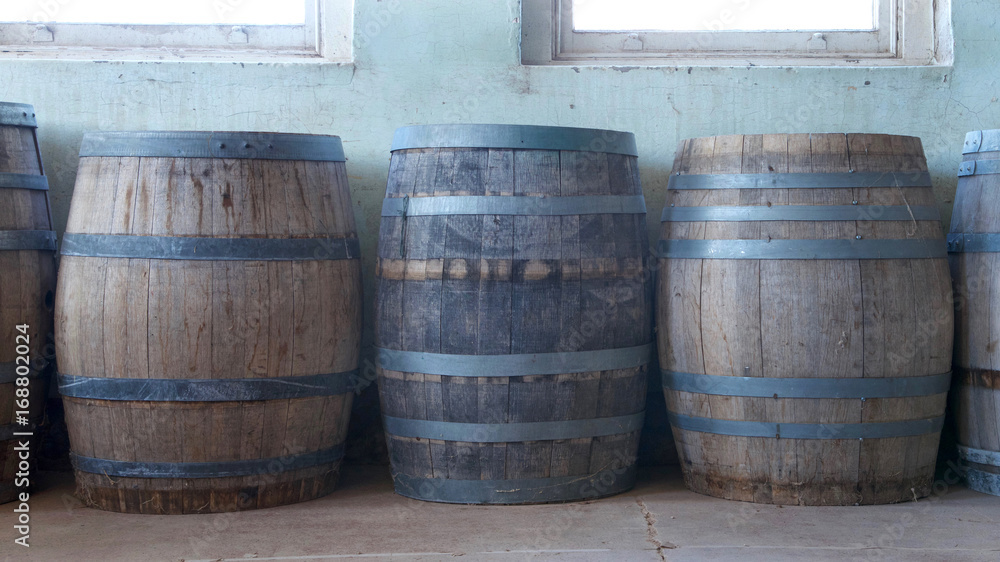 Old wood barrels lining a worn weathered wall in the basement of an old building. Used for food storage in early American history