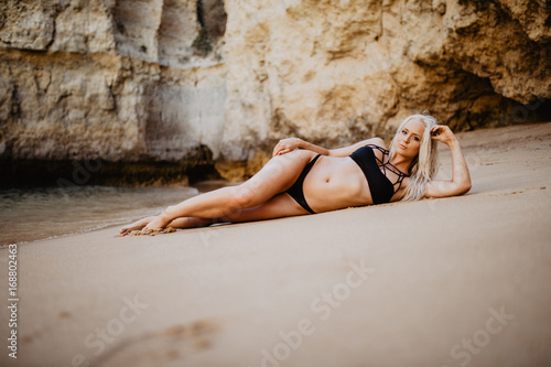 Slim girl wear bikini, lying on a sandy beach with wild waves, horizontal and full body length photo photo