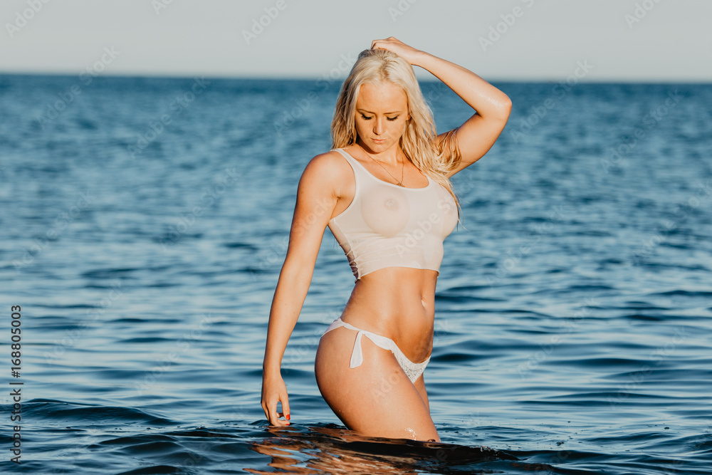 Sexy woman in wet t-shirt playing on water at beach over sea. 