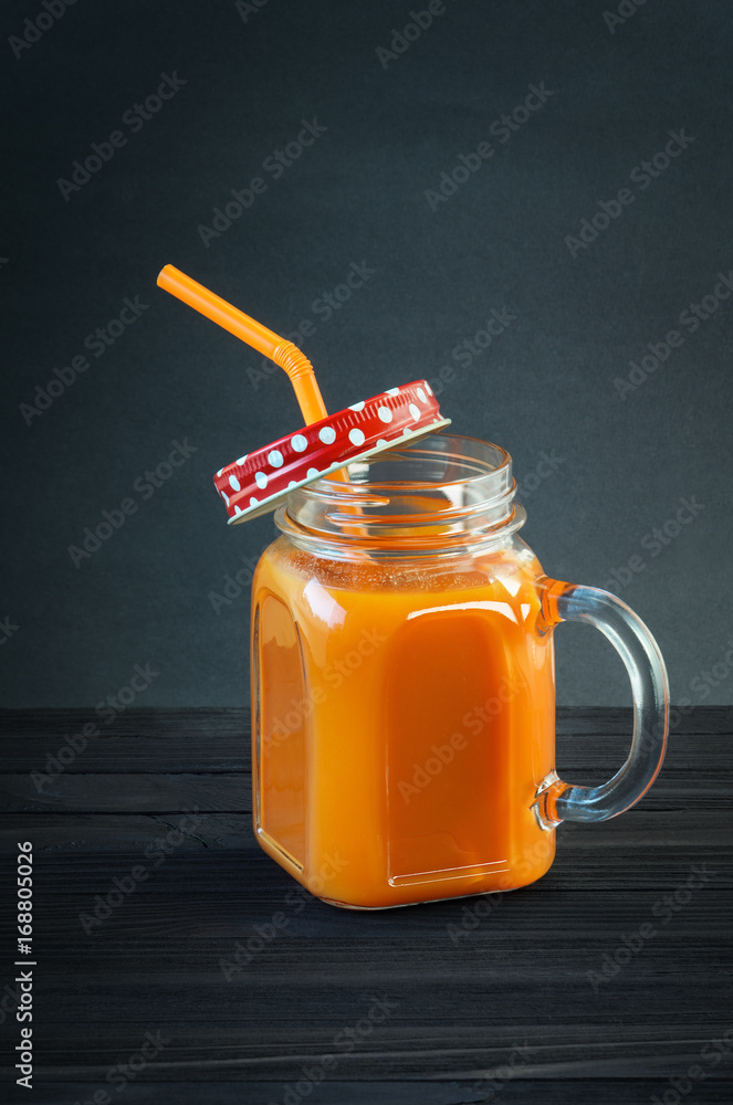 Fresh carrot juice in a glass jar with handle on a black wooden table. Carrot smoothie in a glass mug with a red lid in a white polka dots and an orange straw Fresh carrot juice in a glass jar with handle on a black wooden table. Carrot smoothie in a glass mug with a red lid in a white polka dots and an orange straw