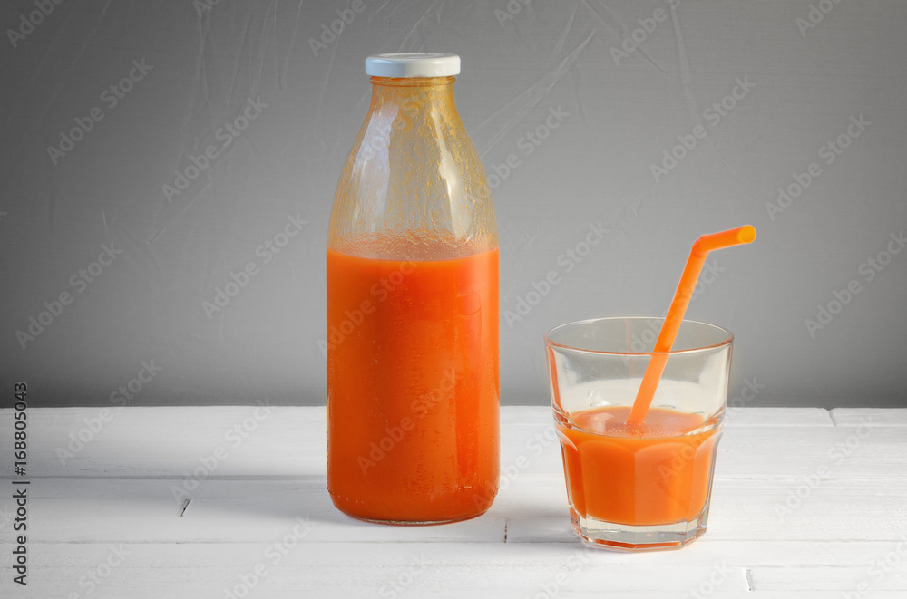 A bottle of carrot juice and a glass of carrot juice with a straw on white wood table. Still life of a healthy eating concept A bottle of carrot juice and a glass of carrot juice with a straw on white wood table. Still life of a healthy eating concept