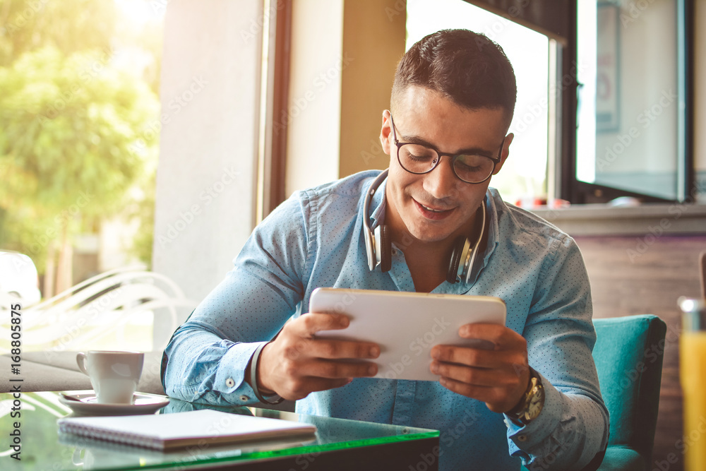 Handsome young businessman is using a tablet and smiling, sitting at bar counter in a modern urban cafe Handsome young businessman is using a tablet and smiling, sitting at bar counter in a modern urban cafe