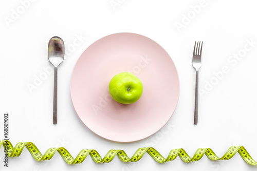 Slimming diet. Apple at plate and measuring tape on white background top view