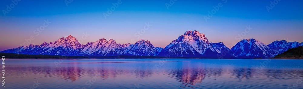 The majestic Grand Tetons in Wyoming remain clad in snow although spring has arrived. The beauty of these mountains is captured also as a reflection in the still blue fresh Jackson Lake. 