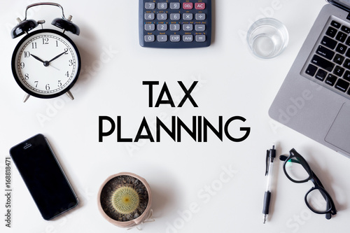 Tax Planning words written on white table with clock, smartphone, calculator, pen, cactus, glass and laptop