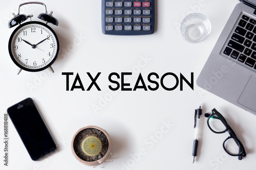 Tax Season words written on white table with clock, smartphone, calculator, pen, cactus, glass and laptop
